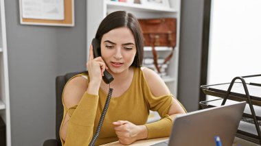 İspanyol kadın modern ofiste telefonla konuşuyor, profesyonellik gösteriyor ve odaklanıyor.