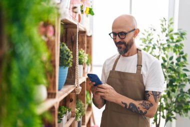 Çiçekçiye akıllı telefon kullanarak gülümseyen kel bir çiçekçi.