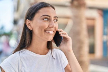 Genç, güzel, İspanyol bir kadın gülümsüyor ve caddede akıllı telefondan konuşuyor.