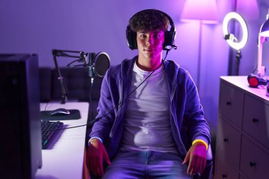 Genç İspanyol asıllı genç oyuncu, gülümsüyor. Oyun odasında sandalyeye oturmuş kendine güveniyor.