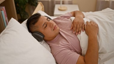 Sıcak sabah titreşimleri, yatakta rahatça uzanan, kulaklık takan, yatak odasında dinlendirici müzik eşliğinde uyuyan Latin bir adam.