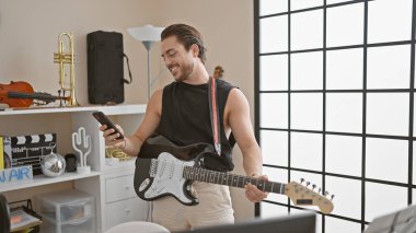 Genç İspanyol müzisyen müzik stüdyosunda akıllı telefon kullanarak elektro gitar çalıyor.