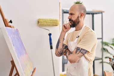 Young bald man artist looking draw with serious expression at art studio
