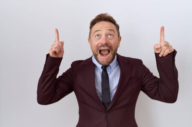 Orta yaşlı, sakallı, kravatlı, şaşkın, şaşkın, parmaklarıyla işaret eden ve kollarını kaldıran bir iş adamı.. 