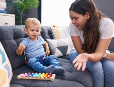 Anne ve oğlu kanepede oturup ksilofon çalıyorlar.