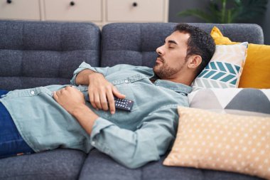 Uzaktan kumandalı İspanyol bir adam kanepede uzanıyor ve evde uyuyor.