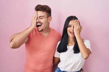 Pembe arka planda duran genç İspanyol çift bir gözünü eliyle kapatıyor, yüzünde kendine güvenen bir gülümseme ve sürpriz bir duygu var.. 