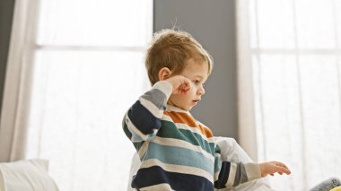 Çizgili tişörtlü çocuk parlak yatak odasında yorgun görünüyor.