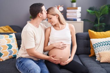 Kadın ve erkek, evdeki koltukta oturarak göbeğe dokunuyor.