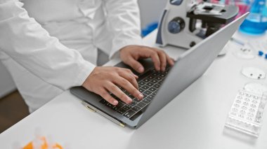 Laboratuvarda mikroskop ve teçhizatlı laptop kullanan laboratuvar önlüklü bilim adamları görülüyor..