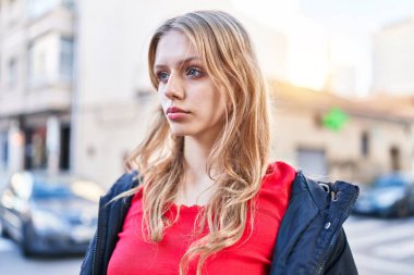 Sokakta ciddi bir ifadeyle yan tarafa bakan genç sarışın kadın.