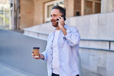 Young caucasian man talking on the smartphone drinking coffee at street