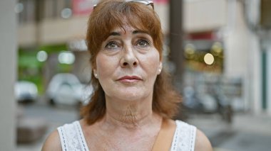 Yetişkin, kızıl saçlı bir kadın işlek bir şehirde düşünceli görünüyor..