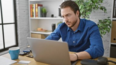 Genç İspanyol iş adamı ofiste dizüstü bilgisayar kullanarak belge okuyor.