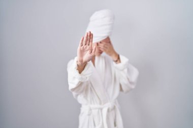 Sarışın, beyaz kadın, bornoz giyiyor, elleriyle gözlerini kapatıyor ve üzgün ve korku ifadeleriyle jest yapıyor. utangaç ve olumsuz kavram. 