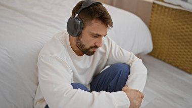 Genç İspanyol adam yatak odasında yerde oturmuş müzik dinliyor.