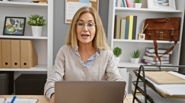 Profesyonel olgun bir kadın kapalı bir ofiste çalışıyor. Güven ve deneyim yayıyor..