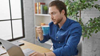 Genç İspanyol iş adamı ofiste kahve içmek için dizüstü bilgisayar kullanıyor.