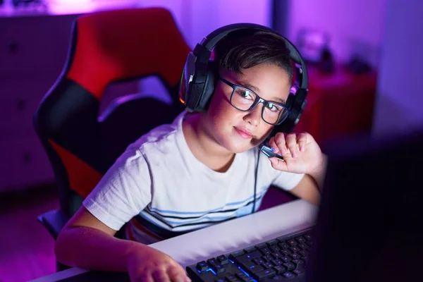 Adorable hispanic boy streamer playing video game using computer at gaming room