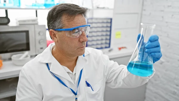Científico Maduro Examina Líquido Azul Frasco Laboratorio Usando Gafas Protectoras — Foto de Stock