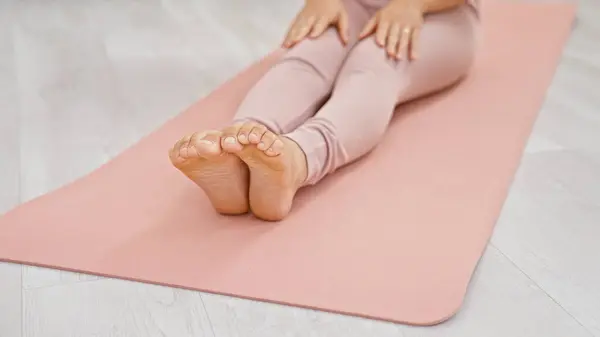 A woman practices yoga on a pink mat in a brightly-lit indoor space, exemplifying health and relaxation.