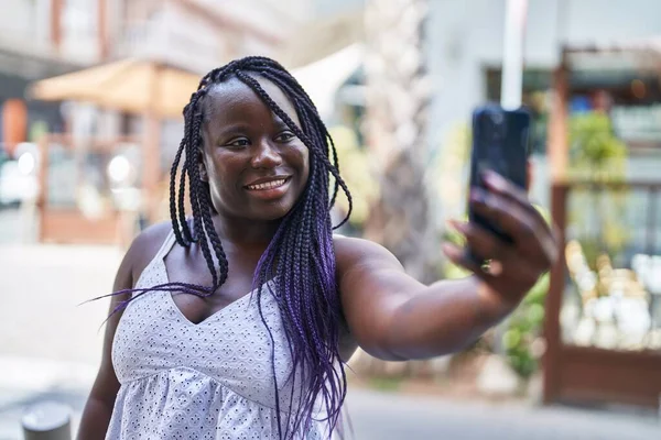Afro-Amerikalı kadın gülümsüyor. Sokakta akıllı telefonun yanında özçekim yapıyor.