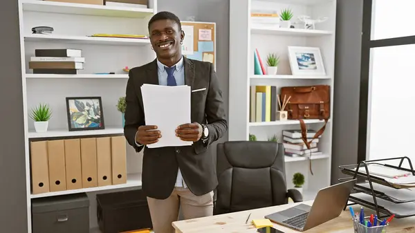アフリカ系アメリカ人がオフィスのインテリアで笑顔で文書を保持 — ストック写真