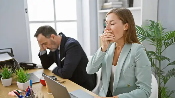 Two exhausted business workers yawning together, signifying long hours of collaborative work at office