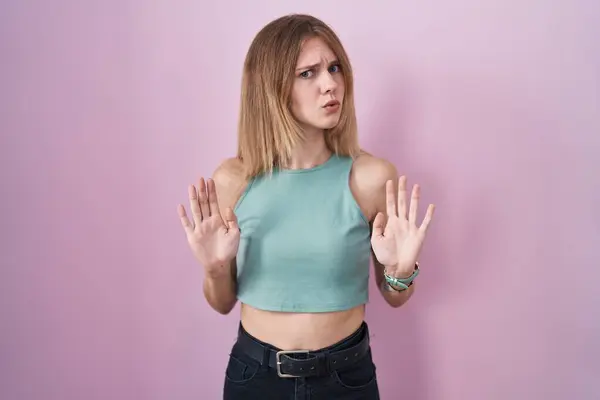 ピンクの背景の上に立つ金髪の白人女性は 恐怖と嫌な表情で拒否と否定を示す手のひらを離れて移動します 止めて禁止する — ストック写真