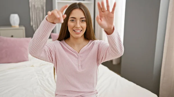 A smiling woman in pink pajamas stretching her arms in a bright bedroom