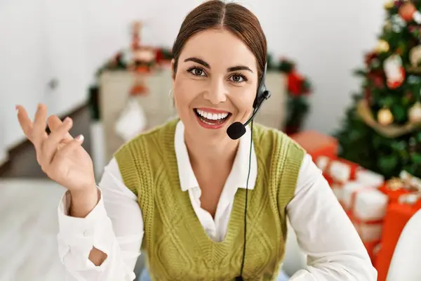 Young beautiful hispanic woman call center agent sitting by christmas tree speaking at home