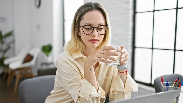 Young blonde woman business worker using laptop drinking water at the office