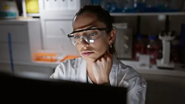 Young beautiful hispanic woman scientist wearing glasses using computer thinking at laboratory