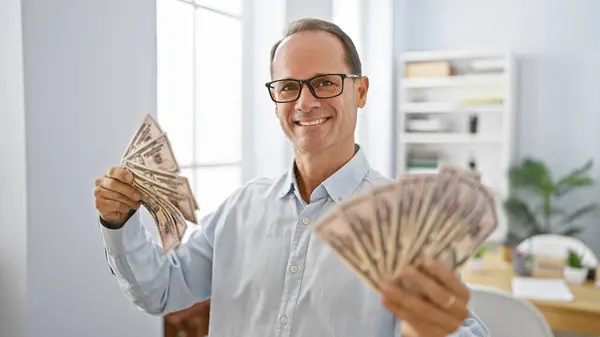 Smiling middle age man confidently handling dollars in his office, a happy worker showcasing success in business