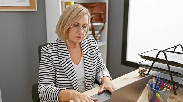 Mature Blonde Woman Striped Blazer Working Laptop Modern Office Setting — Stock Photo, Image