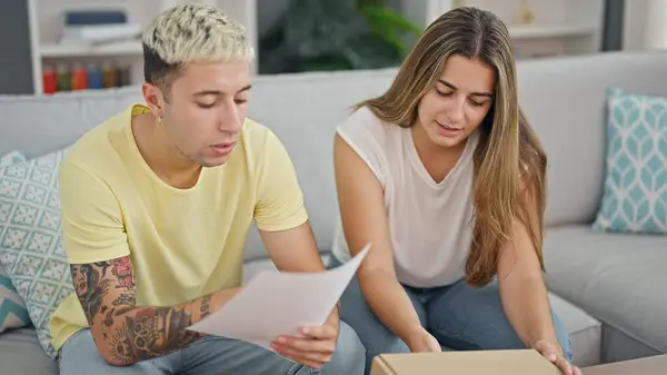 Beautiful couple reading document unpacking cardboard box at home