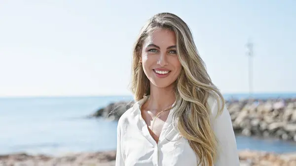 Young blonde woman smiling confident standing at seaside