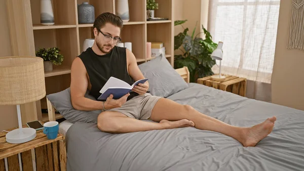 Jonge Spaanse Man Draagt Bril Leesboek Zittend Bed Slaapkamer — Stockfoto