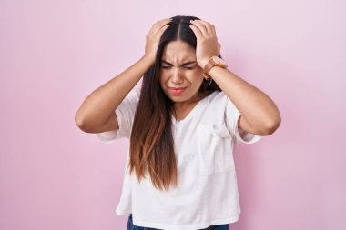 Pembe arka planda duran genç Arap kadın acı ve migren yüzünden çaresiz ve stresli baş ağrısından muzdarip. Eller başının üstünde.. 