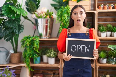 Çiçekçide çalışan genç İspanyol kadın elinde açık tabela ile korkmuş ve ağzı açık şaşkınlık içinde, inançsız bir yüz. 