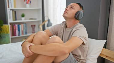 Young hispanic man listening to music relaxed on bed at bedroom