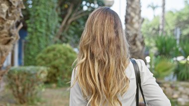 Şehir parkının yeşil doğası gerisinde duran güzel sarışın kadın. Arka plan portresinin çarpıcı portresini çizen sıradan bir yürüyüş..