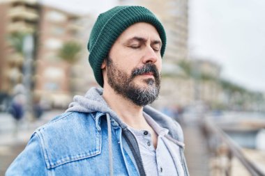 Genç kel adam deniz kenarında gözleri kapalı nefes alıyor.