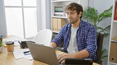 Sarı sakallı, mesleki hayallerini yaşayan, ofis masasında dizüstü bilgisayarla iş yapan, odaklanmış ve gevşemiş bir şekilde başarı için çabalayan Latin asıllı genç bir adam..