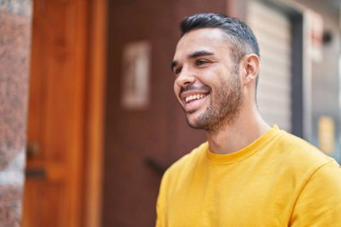 Young hispanic man smiling confident looking to the side at street