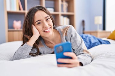 Yatakta uzanmış akıllı telefon kullanan genç, güzel İspanyol kadın.