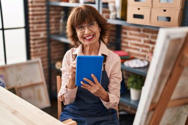 Sanat stüdyosunda dokunmatik ped kullanan orta yaşlı kadın sanatçı gülümsüyor.