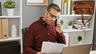 Ofiste sakallı yakışıklı bir İspanyol, evrakları inceliyor, iş ortamını inceliyor.