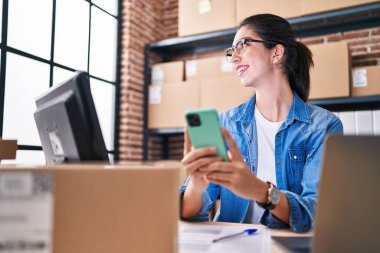 Genç, güzel, İspanyol bir kadın. İş kadını. Ofiste dizüstü bilgisayar ve akıllı telefon kullanıyor.