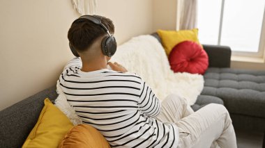 Ses dünyasına kendini kaptırmış çekici, genç İspanyol bir adam, rahat bir şekilde kanepede oturuyor, müzik içinde kaybolmuş, rahat dairesinde kulaklıklarının arkasından bağırıyor..